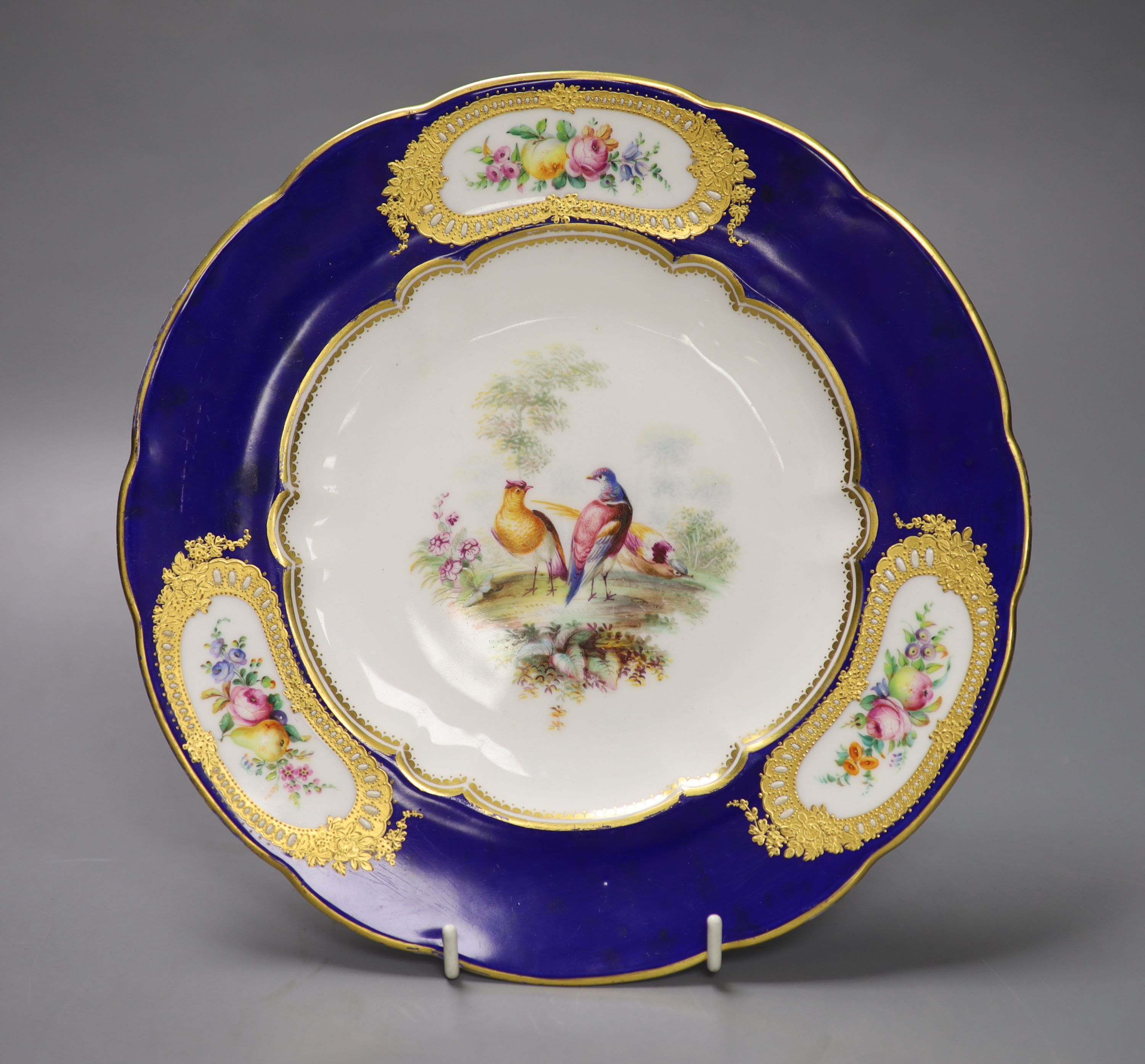 A Coalport plate painted with exotic birds in landscape, the blue border with three raised gilt, jewelled panels painted with fruit and